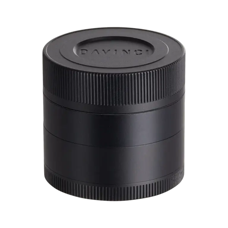 DaVinci herb grinder in matte black, shown closed. A compact, cylindrical four-piece grinder with knurled edges on each section for grip, and the 'DAVINCI' brand name embossed on the flat top lid.
